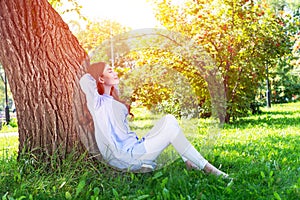 Young woman sitting under tree in summer park