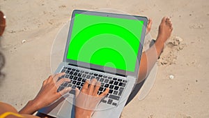 Young woman sitting and using laptop on beach in the sunshine