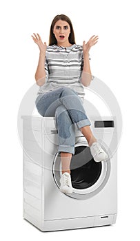 Young woman sitting on washing machine against white background.