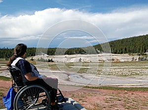 Young woman sitting in wheelchair, observing geysers at Yellowstone National Park