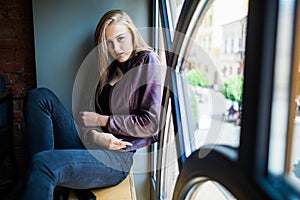 Young woman is sitting on a window sill in a cafe and enjoy free time