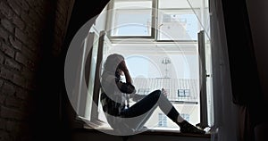 Young woman sitting on window sill and enjoying old town view. Silhouette of relaxing Girl on fresh air at home