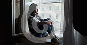 Young woman sitting on window sill and enjoying old town view. Silhouette of relaxing Girl on fresh air at home