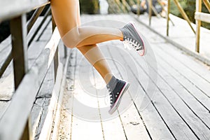 Young woman sitting on a wooden bridge railing in jeans sneakers