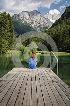 Young woman sitting on wooden footbridge in scenic mountain lake plansarsko, slovenia
