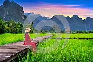 Young woman sitting on wooden path with green rice field in Vang Vieng, Laos