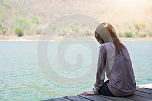 young woman sitting on wooden raft front of herself are blue water background. this image for travel,nature and portrait