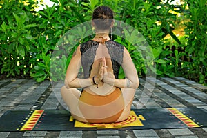 Young woman sitting on yoga mat, meditating, practicing yoga and pranayama. Lotus pose with hands in namaste mudra. View from back