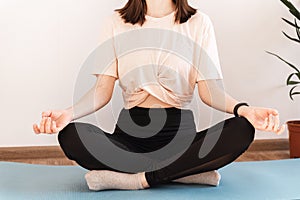 Young woman sitting on a yoga mat and practicing meditation. Relaxation, rest, mental health. Exercises at home in the room