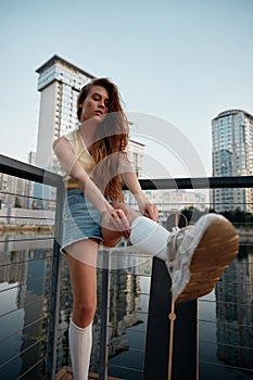 Young woman skateboarder dressed in casual attire taking break