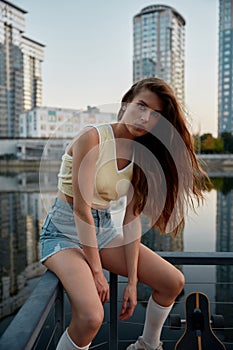 Young woman skateboarder dressed in casual attire taking break