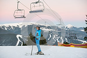 Young woman on ski smiling and showing hand to distance