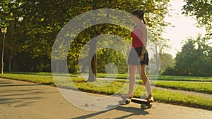 Young woman in a skirt and flip flops riding a skateboard through the park.