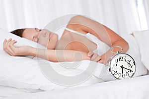 Young woman sleeping in bed with alarm clock