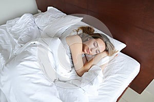 Young woman sleeping in morning on wooden bed with white linens.