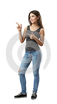 Young woman in sleeveless top and jeans standing in half-turn with both hands bent and index fingers pointing sideward