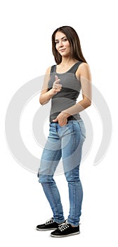 Young woman in sleeveless top and jeans standing in half-turn with left hand in pocket and right hand pointing at viewer