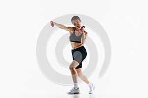 Young woman with slim sportive body training, doing jab exercises with dumbbells isolated over white studio background