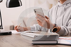 Young woman with smart watch and phone at table in office, closeup