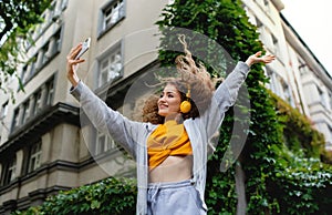 Young woman with smartphone dancing outdoors on street, tik tok concept. photo