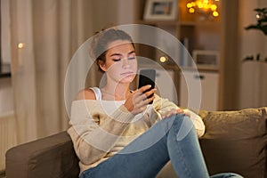 Young woman with smartphone at home in evening
