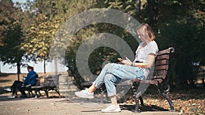 Young woman with a smartphone sitting on a brunch at the autumn park