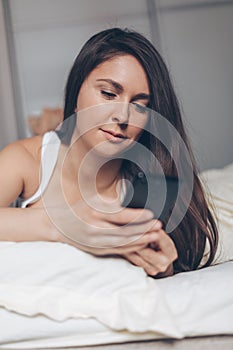 Young woman with smartphone texting message in bed at home