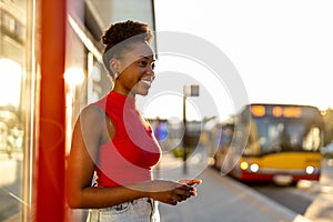 Young woman with smartphone waiting at the bus stop