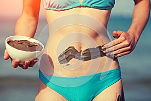 Young woman smearing mud mask on the body