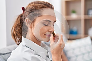 Young woman smelling marihuana bud sitting on sofa at home