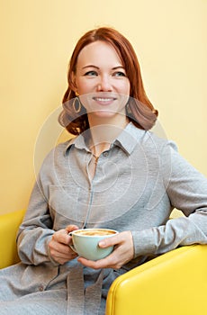 Young woman with a smile in a cafe with a Cup of coffee. A sunshine yellow background.
