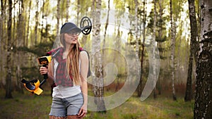 A young woman with smile holding a metal detector over her shoulder in the forest