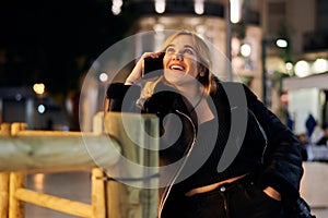 Young woman smiles and calls with her phone in a city at night