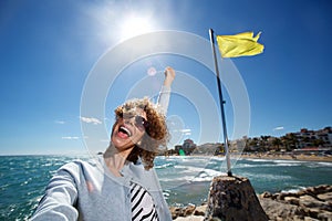 Young woman smiling with arm in air while taking selfie at the beach