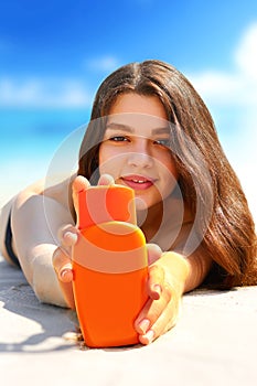 .Young woman smiling on beach and holding sunscreen bottle in her hands