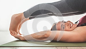 Young Woman smiling into camera enjoying morning yoga exercises doing Halasana pose at home living room . Active people and
