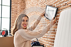 Young woman smiling confident hanging picture on wall at new home