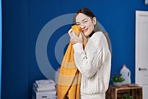 Young woman smiling confident touching with face soft sweater at laundry room