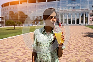 Young woman smiling and drinking cocktail with ice in plastic cup with straw