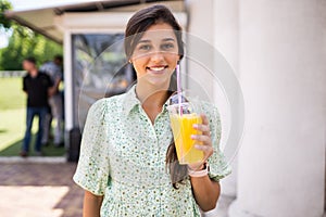 Young woman smiling and drinking cocktail with ice in plastic cup with straw