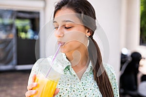 Young woman smiling and drinking cocktail with ice in plastic cup with straw