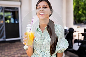 Young woman smiling and drinking cocktail with ice in plastic cup with straw