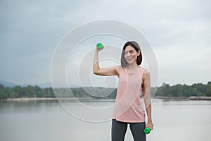 Young Woman Smiling exercising with dumbbell at the park. Healthy Lifestyle concept