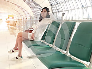 Young woman smiling with green chair sitting in airport hall while waiting landing