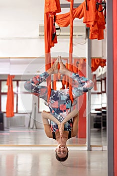 Young woman smiling while hanging from a ceiling, wrapped in hammock and being inverted, aerial yoga