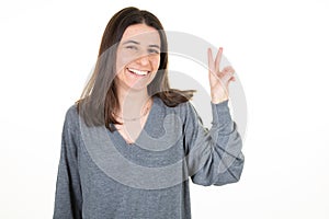 Young woman smiling happy sucess showing two fingers v positive and peace gesture white background