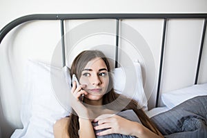 Young woman smiling with her mobile phone on bed talking and texting