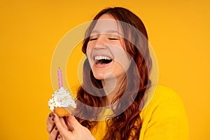 Young woman smiling while holding a birthday cupcake.