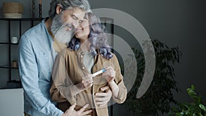 Young woman smiling holding pregnancy test while husband hugging and kissing expressing love