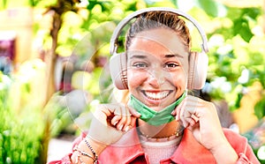 Young woman smiling looking at camera with open facial mask and headphones - New normal lifestyle concept with millenial girl photo